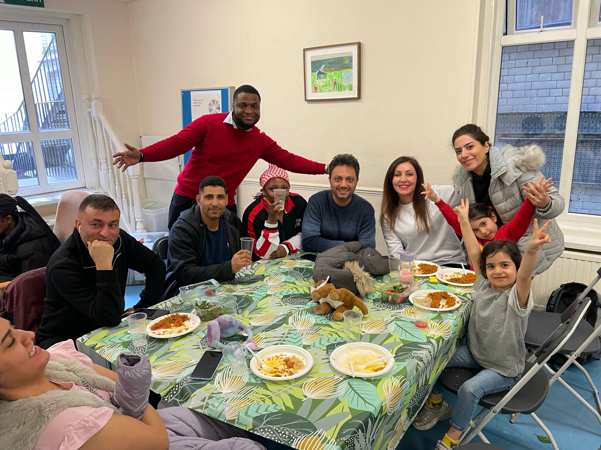 Clients at drop in Erwachsene und Kinder sitzen an einem Tisch im Flüchtlingszentrum und essen gemeinsam.